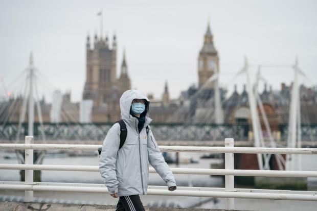 A person wearing a face mask crosses Waterloo Bridge, in London