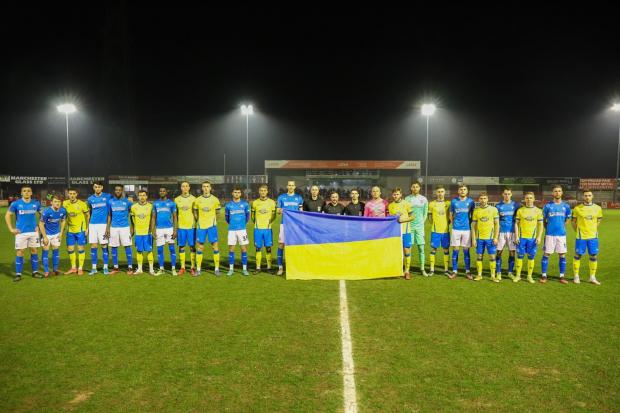 UNITED FRONT: The two teams line up behind a Ukraine national flag before kick-off. Picture by Jonathan Moore